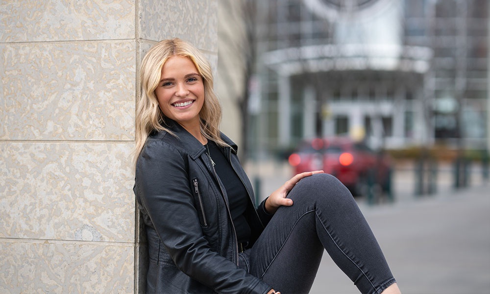 Amanda leans against a tiled wall outside of Building 6